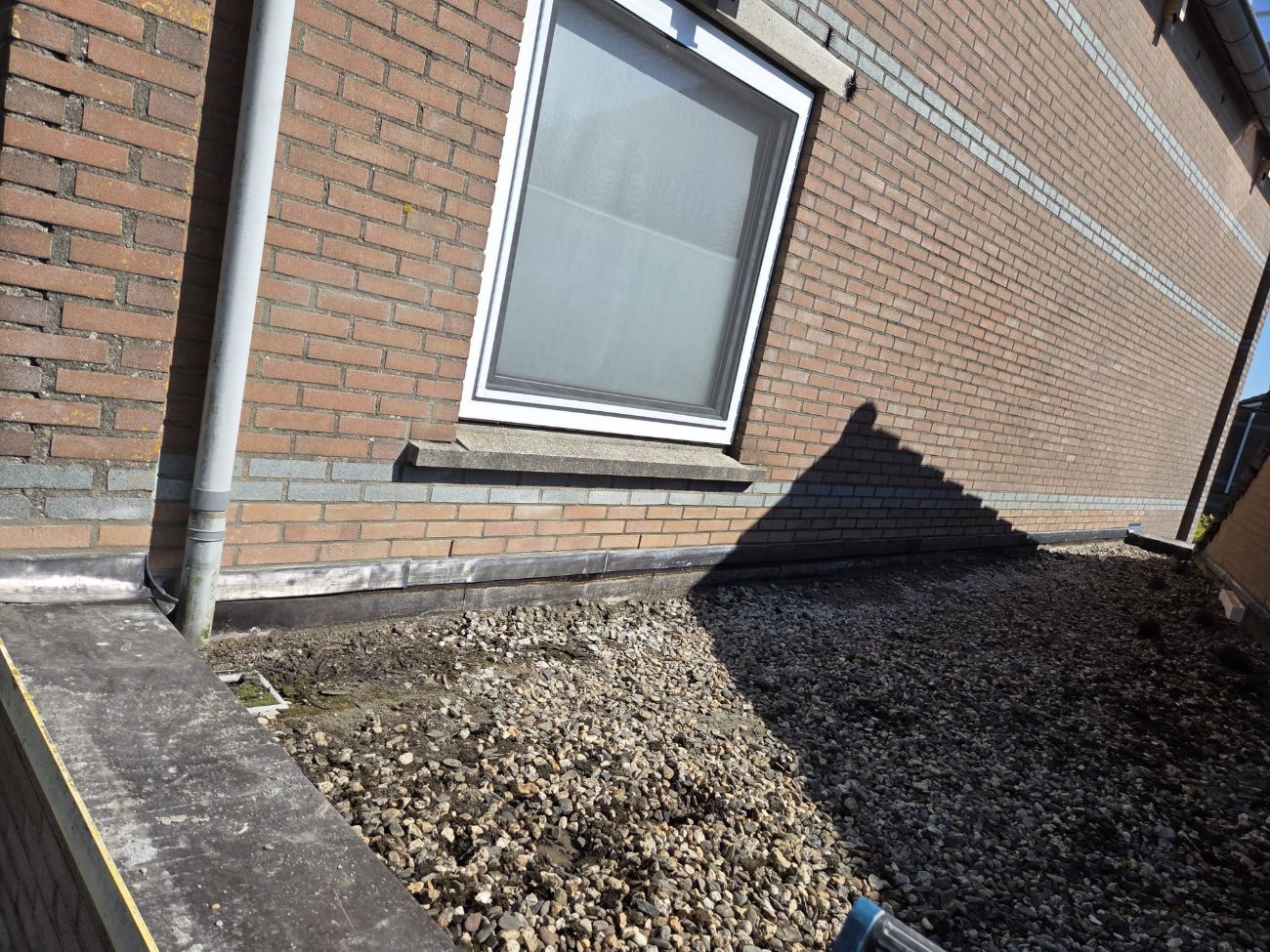 Loodopstand tegen een bakstenen muur op een plat dak, in zonlicht.