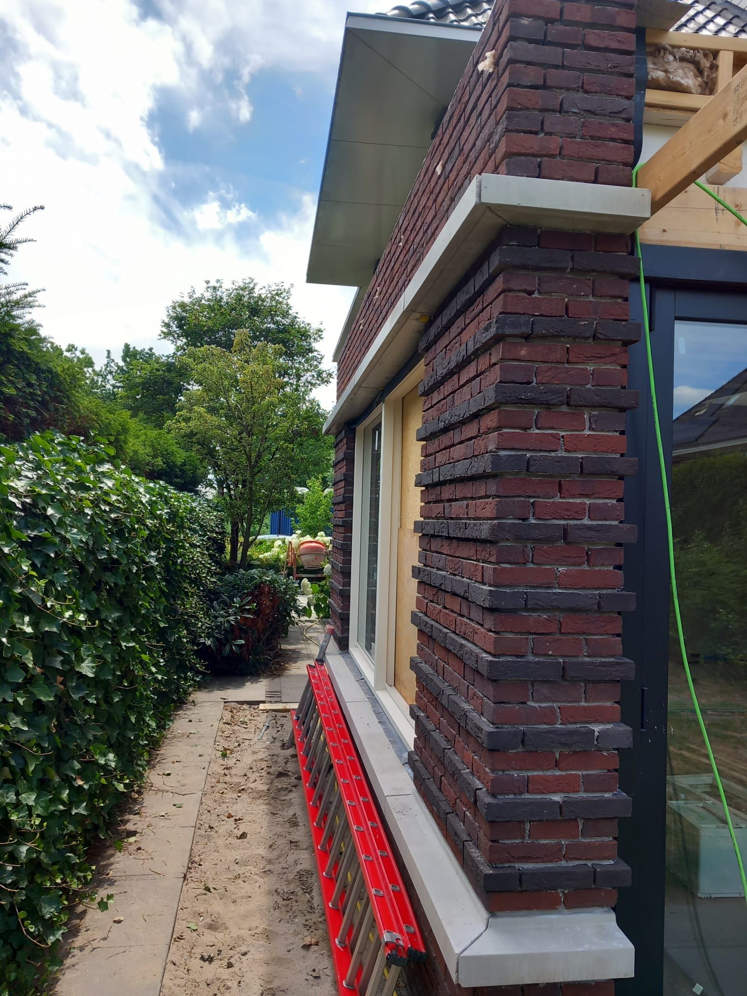 Hoek van een aanbouw met nieuw metselwerk in rood-bruine baksteen en natuurstenen onderdorpels.