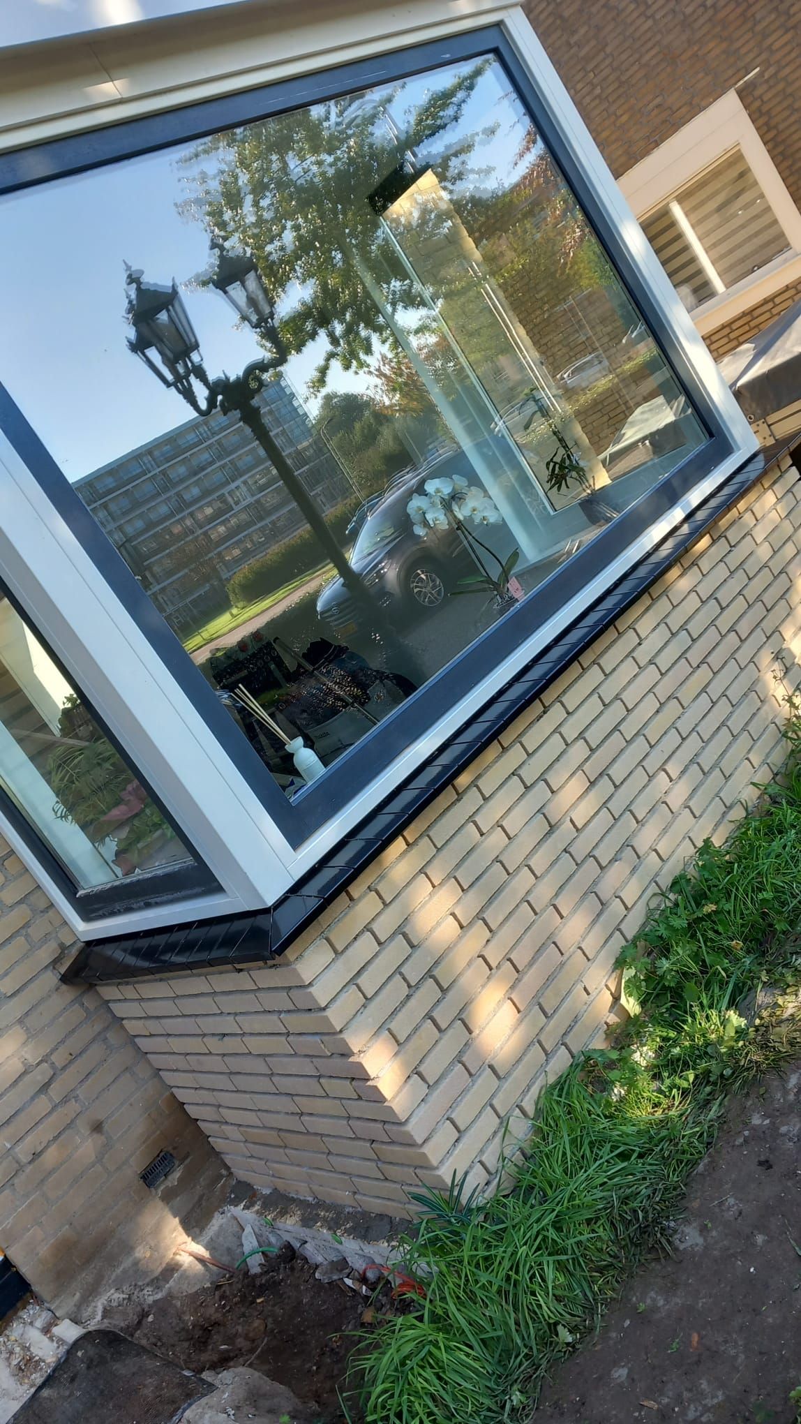 Nieuwe donkere raamdorpels langs een groot hoekvenster, met nieuw metselwerk in lichte baksteen eronder.