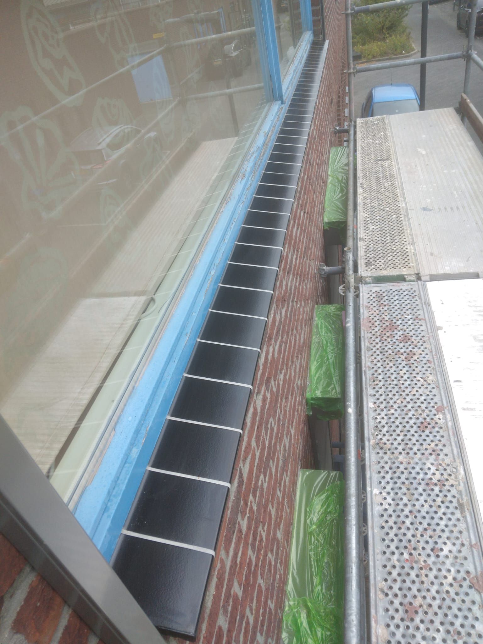 Lange rij nieuwe donkere raamdorpels onder de vensters van een bakstenen gevel, gezien vanaf een steiger.