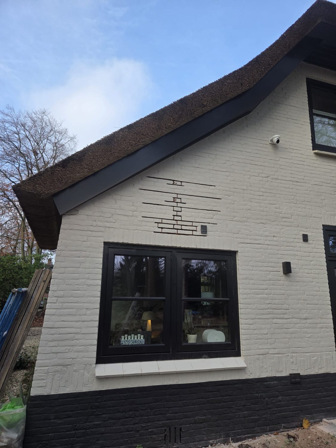 Bakstenen topgevel van een wit geschilderde woning met rieten dak, met boven het venster een trapsgewijze lijn in het metselwerk.