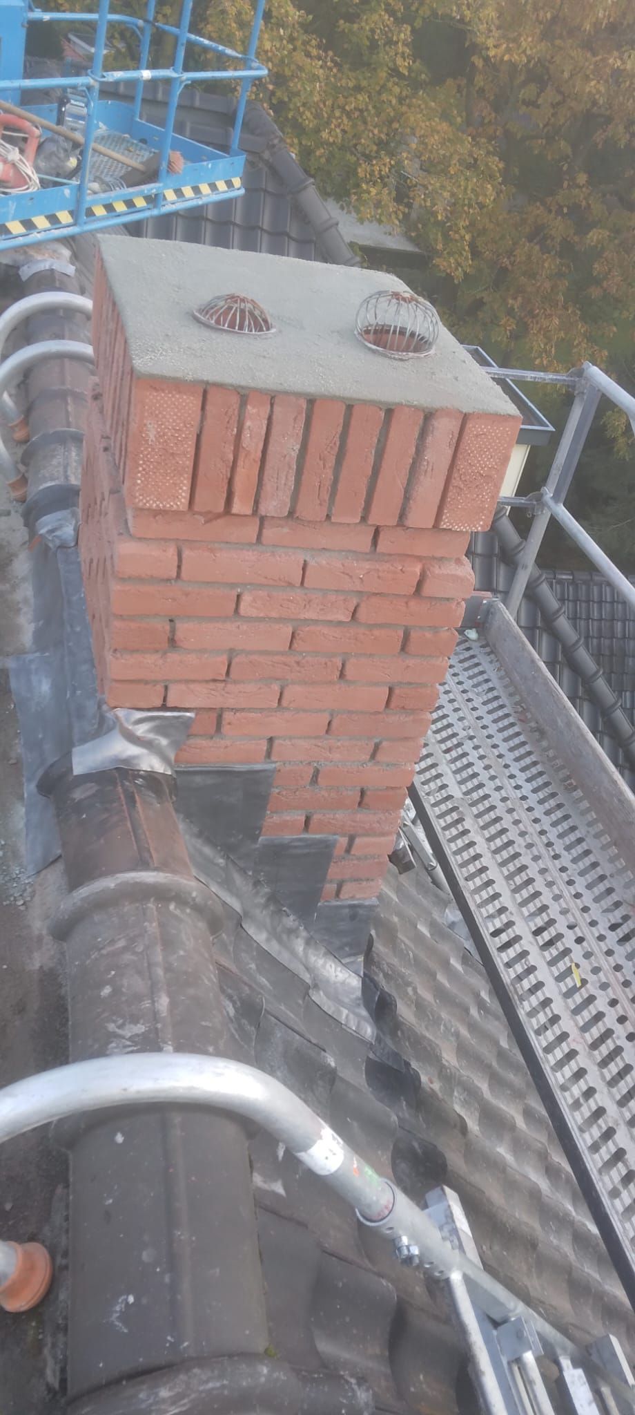 Schoorsteen met nieuw metselwerk, een afdekplaat en twee ronde dakkappen, gezien vanaf het dak.