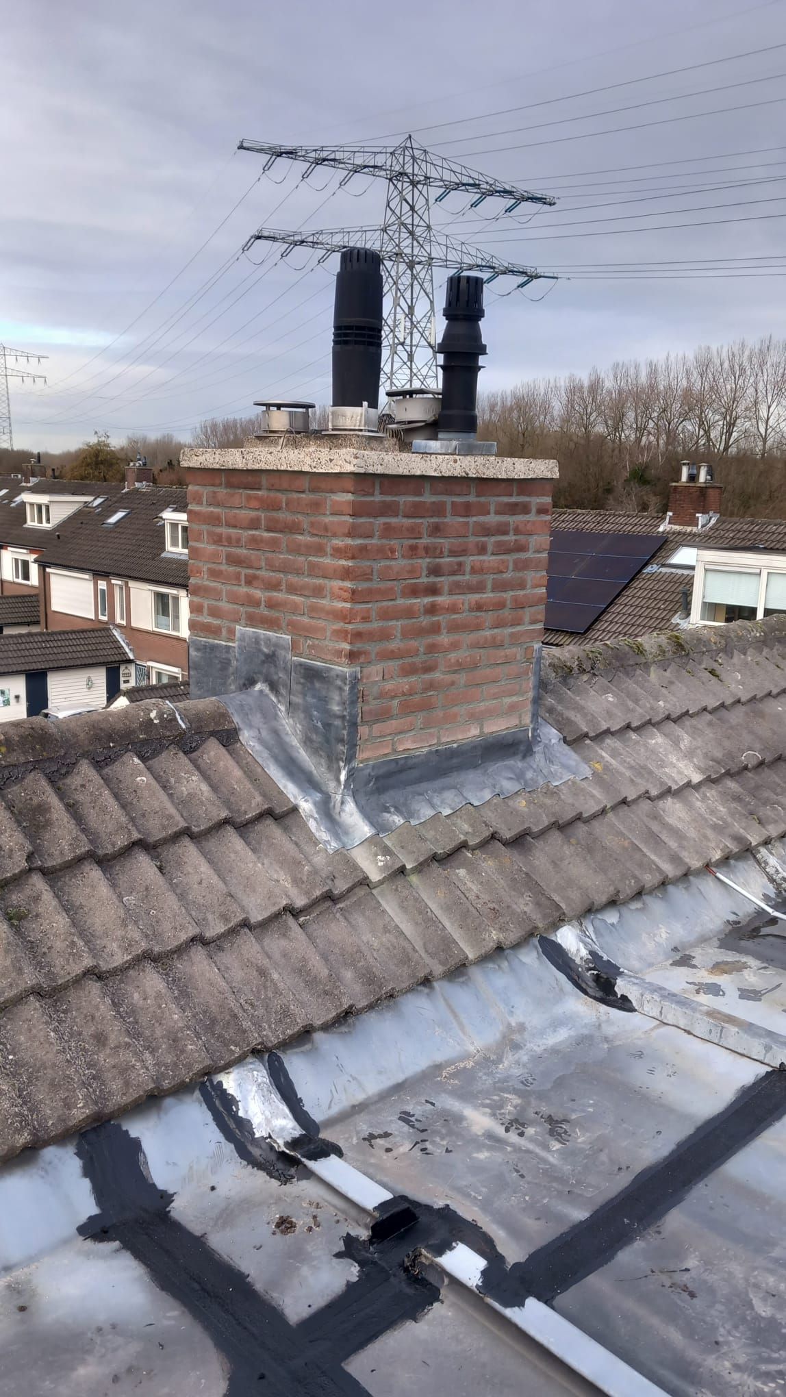 Bakstenen schoorsteen met nieuw loodwerk aan de voet, op een pannendak.