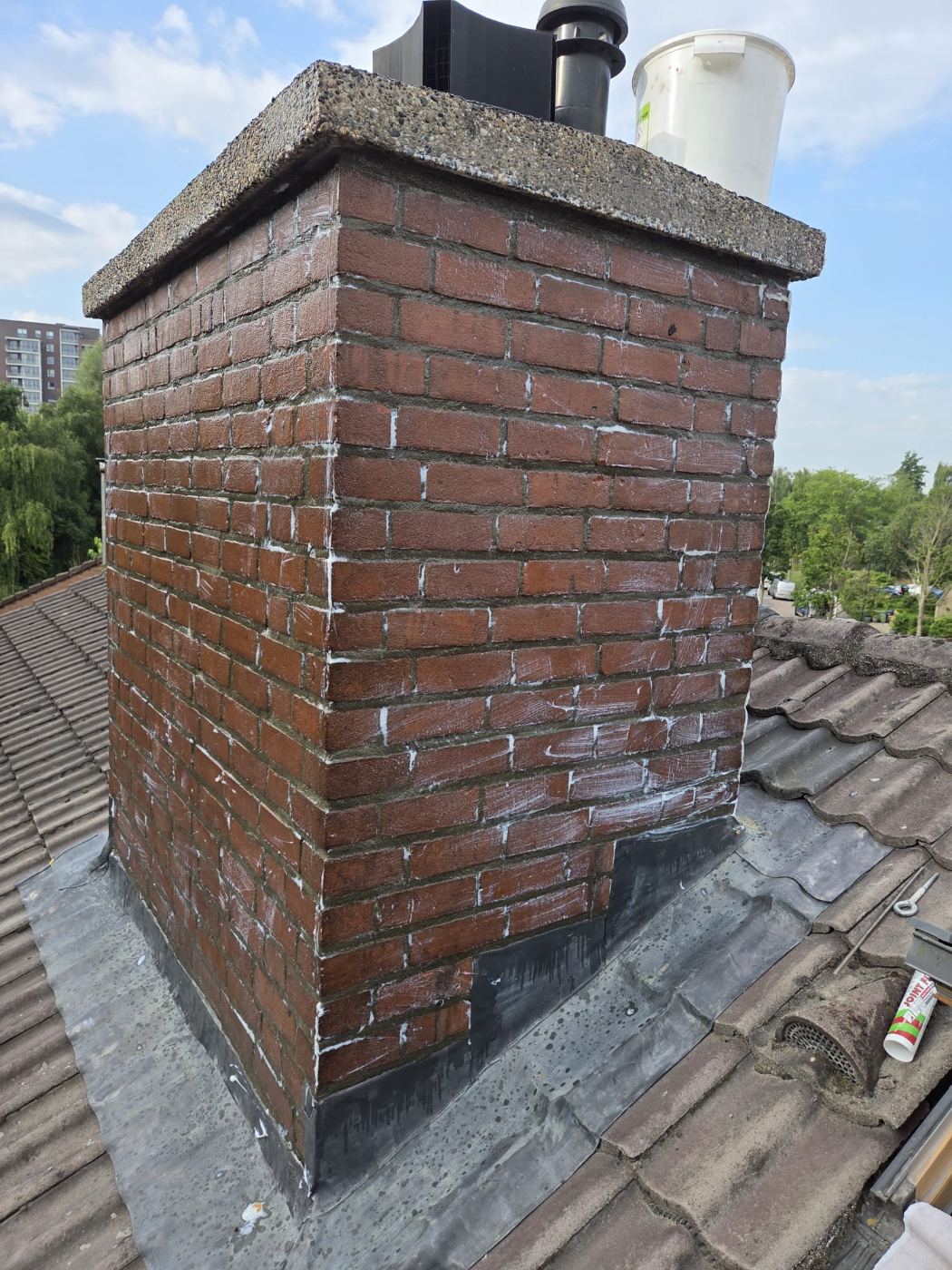 Gerenoveerde bakstenen schoorsteen op een pannendak met nieuw voegwerk en nieuw ringlood