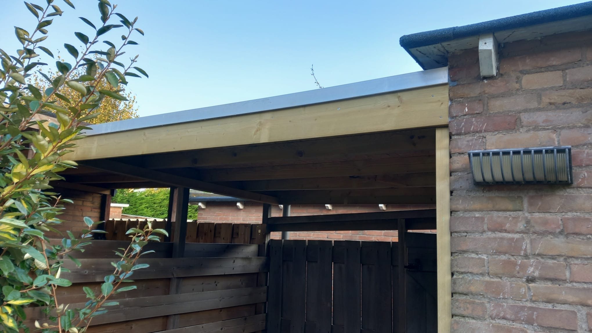 Houten overkapping met plat dak tegen de achtergevel van een woning.
